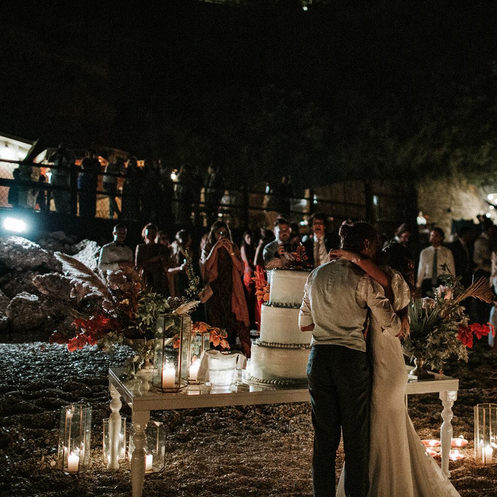 Bride and cutting their wedding cake on the beach with lanterns and dried flower decor 