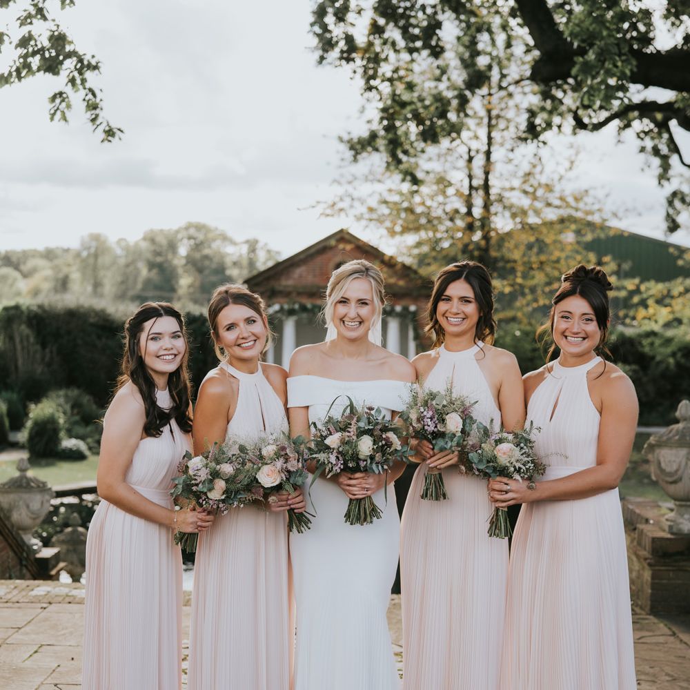 Bride stands with her bridesmaids who are wedding blush pink H&M dresses