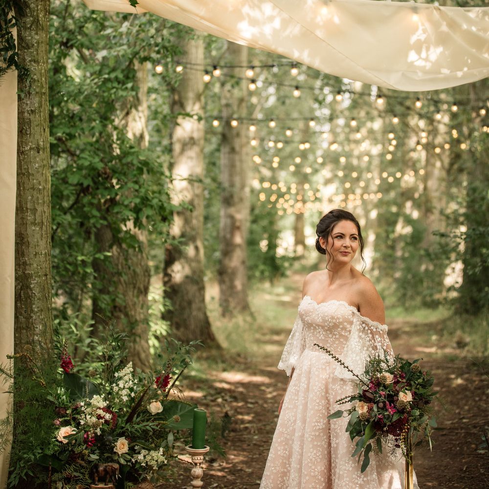 Bride stands under fairy lit line of trees