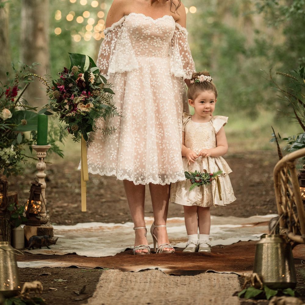 Bride stands with little girl whilst holding floral bouquet