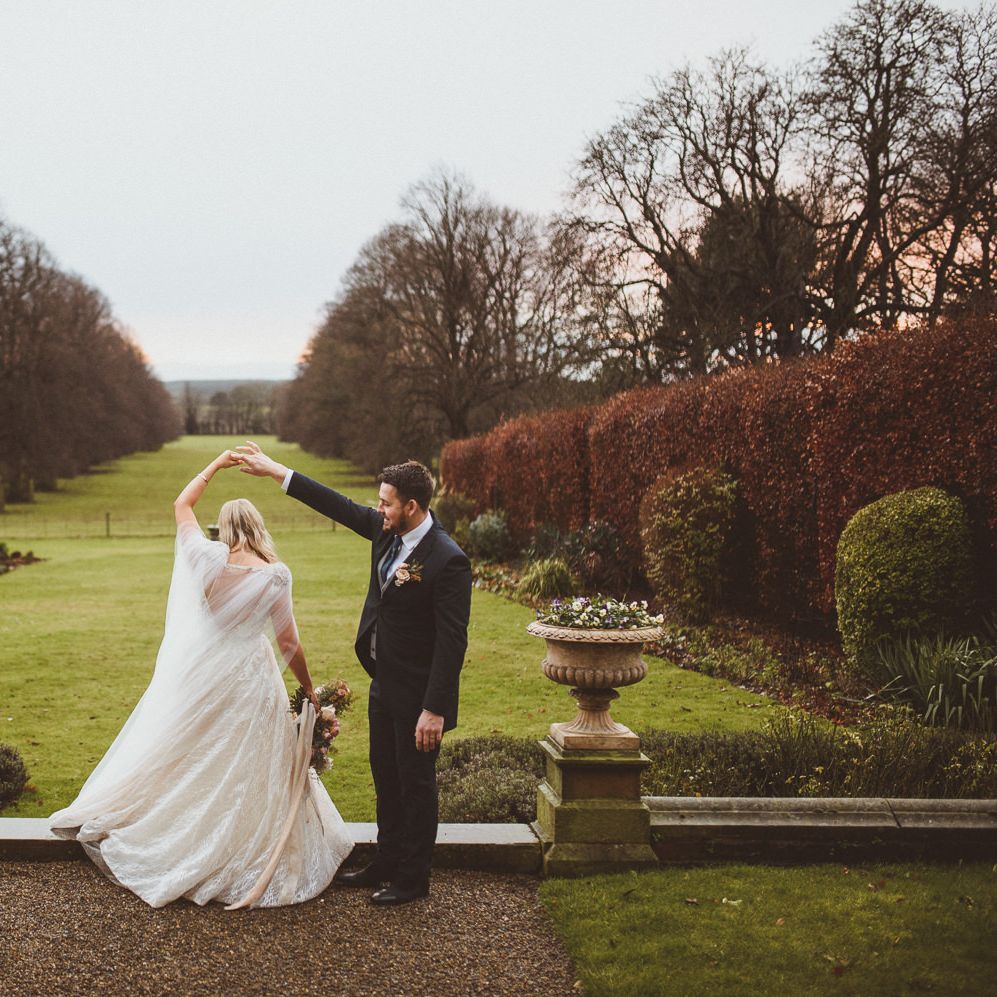 Groom in wedding tails twirling his bride in a princess wedding dress and cape at Goldsborough Hall wedding venue 