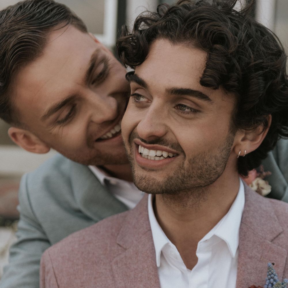 Grooms embrace outdoors whilst smiling lovingly