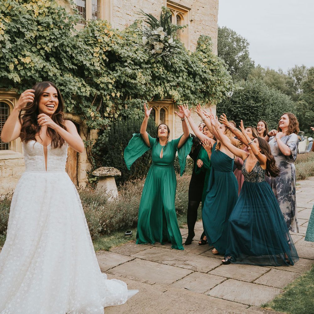 Bride in white Pronovias wedding dress and Jimmy Choo wedding shoes throws white and green bridal bouquet to bridesmaids in green bridesmaid dresses and wedding guests at Notley Abbey wedding
