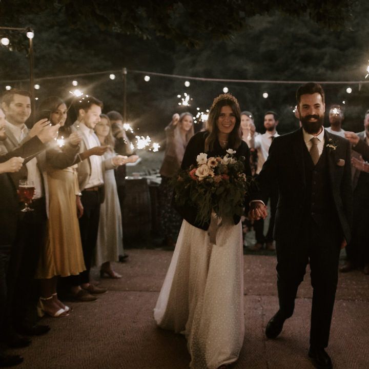 Bride & groom stand with their wedding party who hold sparklers