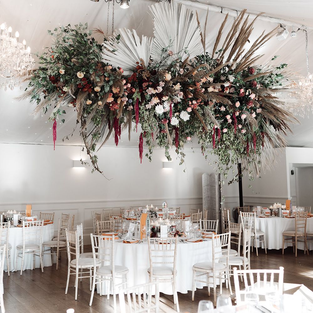 Wedding reception with hanging floral installation including dried and fresh flowers and palm leaves