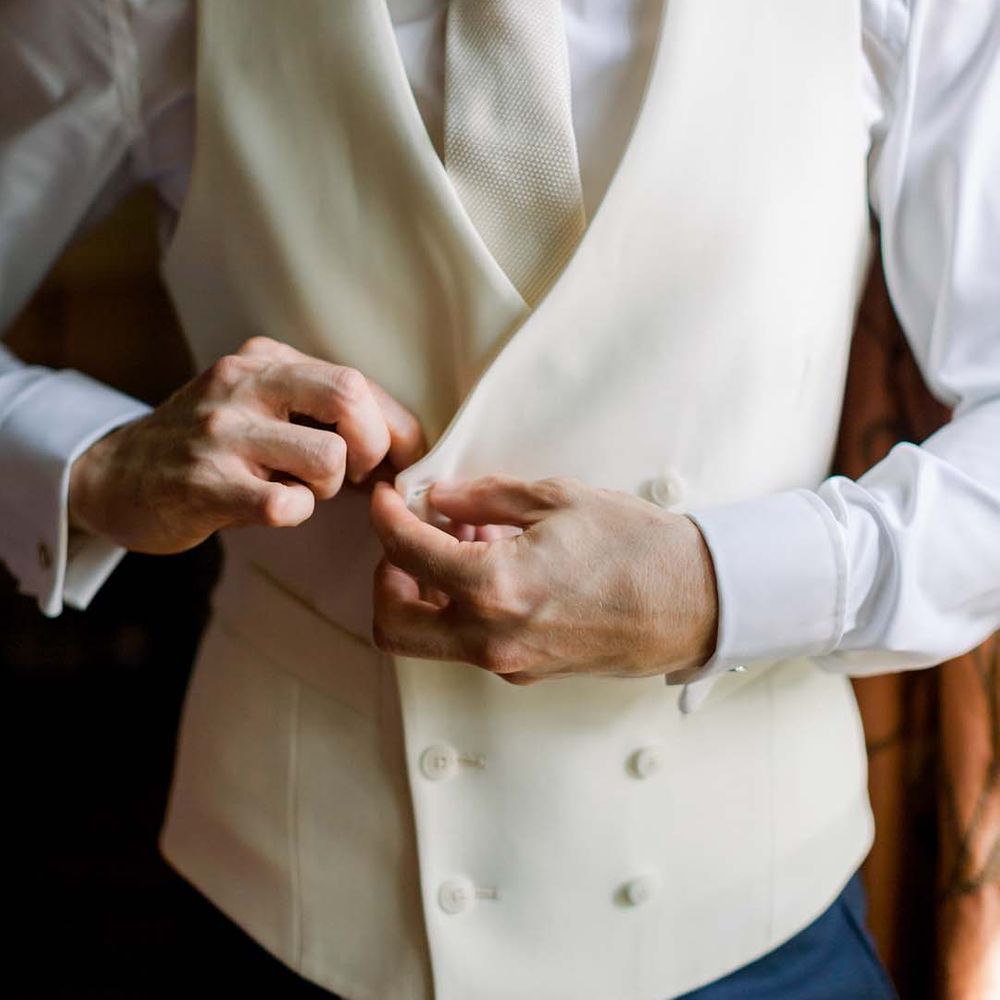 Groom does up his waistcoat on his wedding day