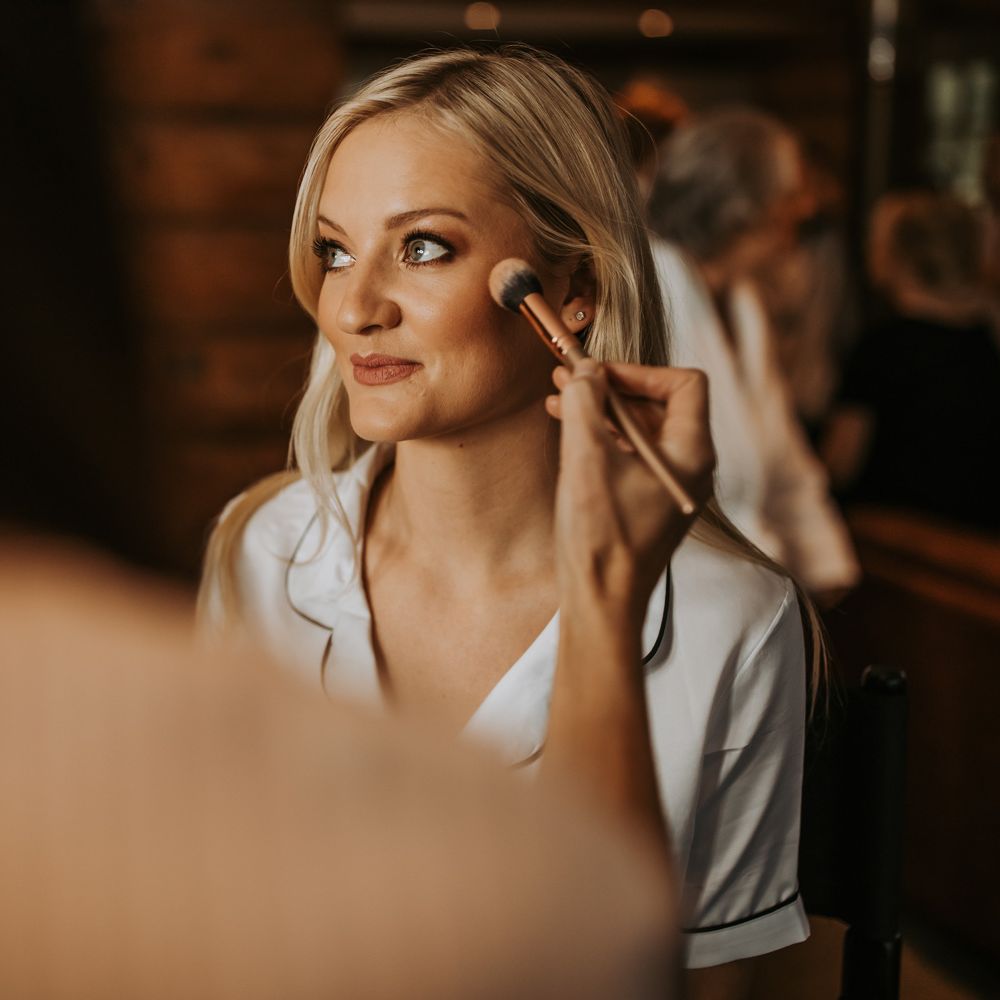 Bride in satin pyjamas has her make up done before barn wedding