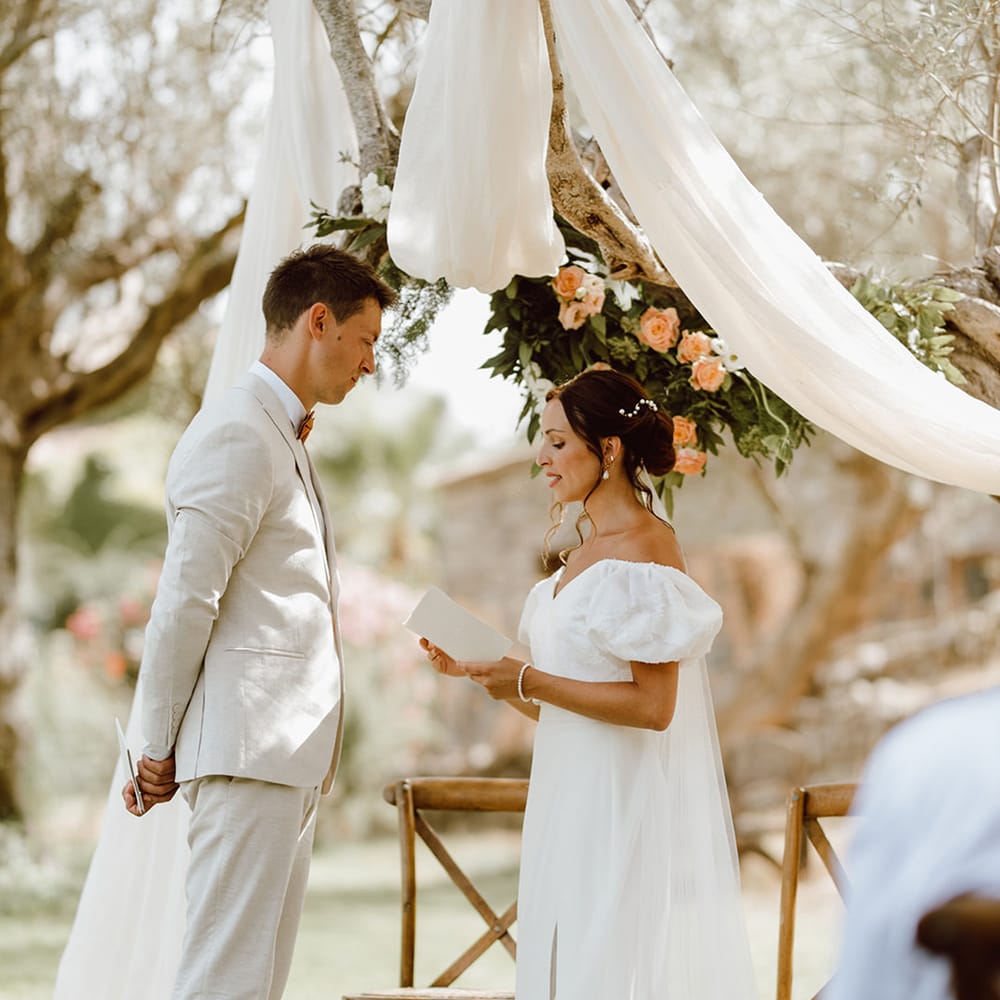 Bride in puff sleeve dress reads wedding vows to husband in beige suit 