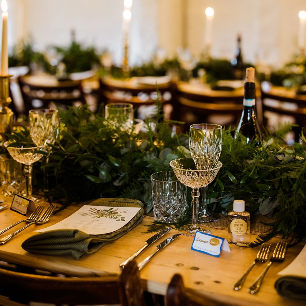 Tablescape with green foliage runner and green napkins with crystal glassware and mini antibacterial gels 