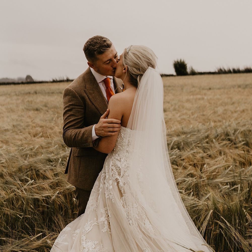 Bride in strapless sweetheart wedding dress with veil kisses groom in autumnal style suit 
