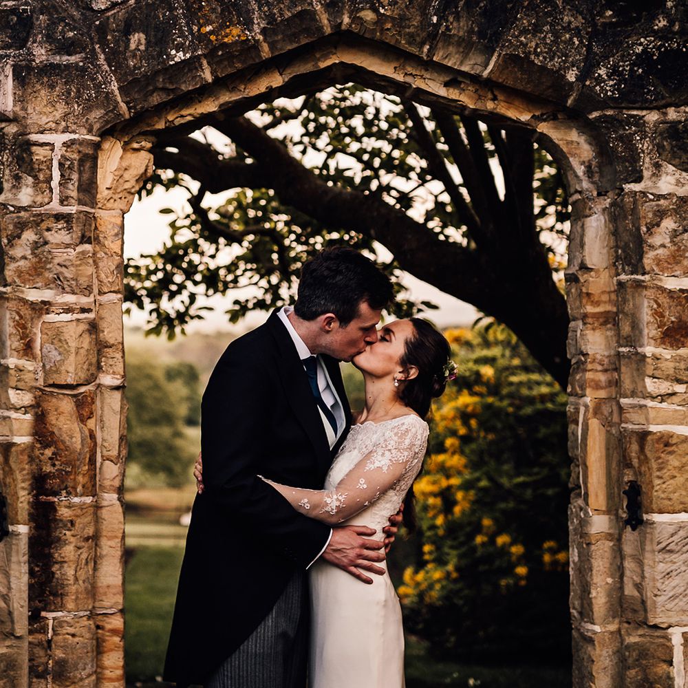 Bride and groom kiss under an archway on their wedding day 