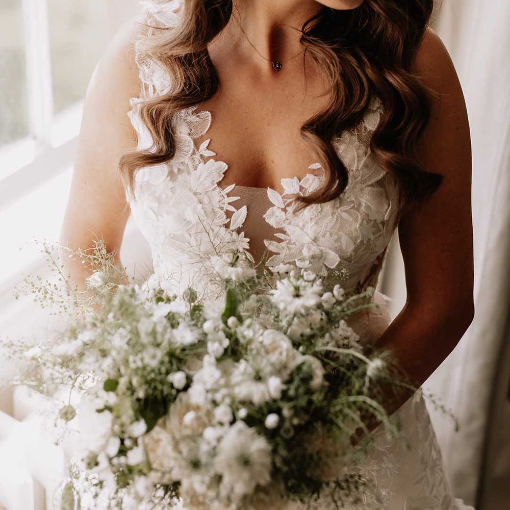Bride with white wedding bouquet in floral wedding dress with diamanté gold earrings 