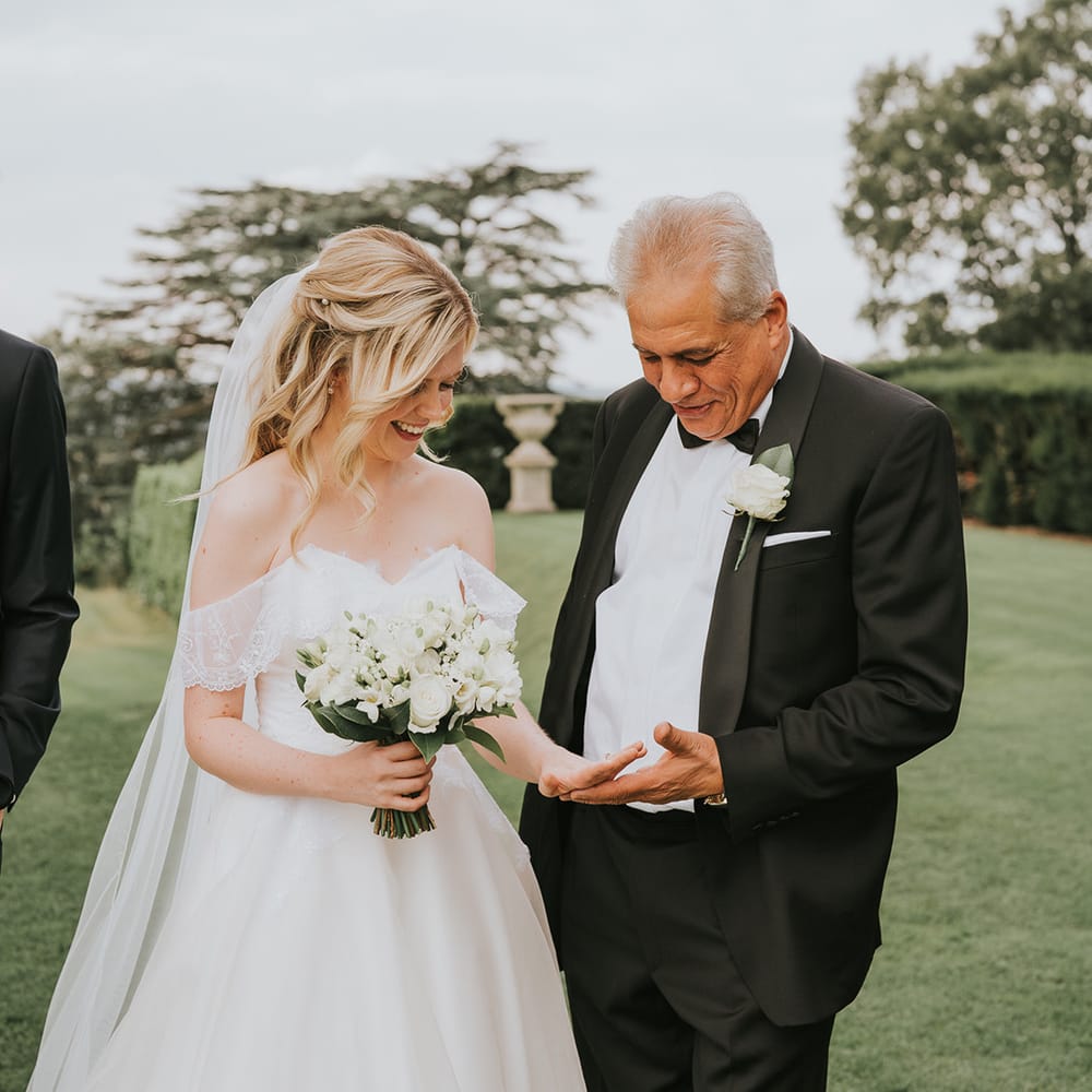 Bride in off the shoulder wedding dress shows off her ring to wedding guest in black tie 