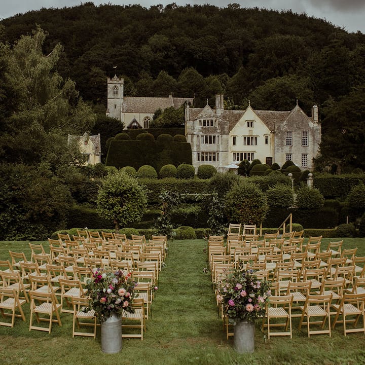 Outdoor wedding ceremony setup at Owlpen Manor with wooden chairs and pink wedding flowers 