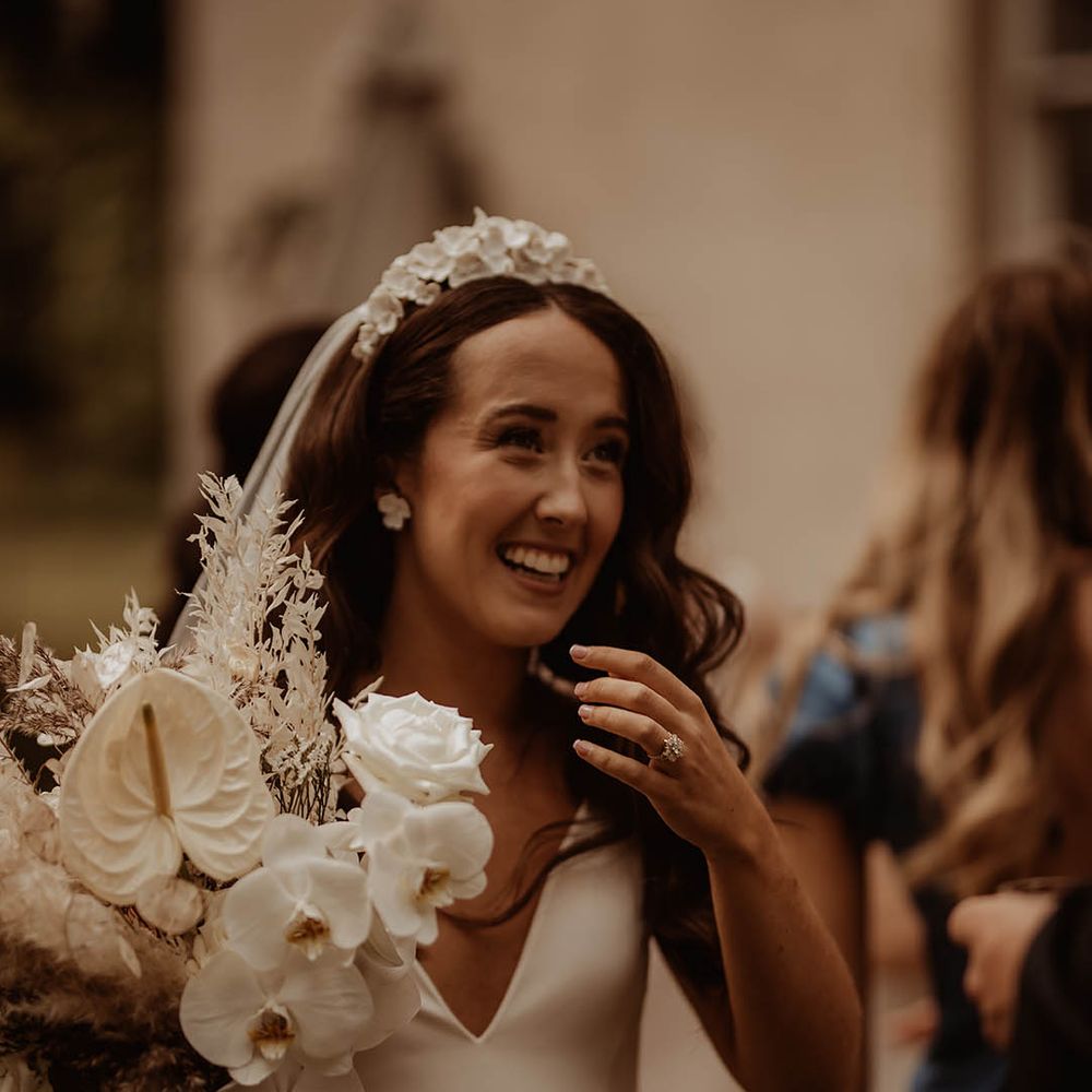 Bride holding an orchid bridal bouquet with white flower earrings and bridal headband in v neck wedding dress