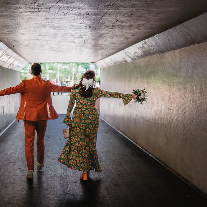 Bride & groom lift their arms and walk through tunnel as bride lifts her bouquet in the air 