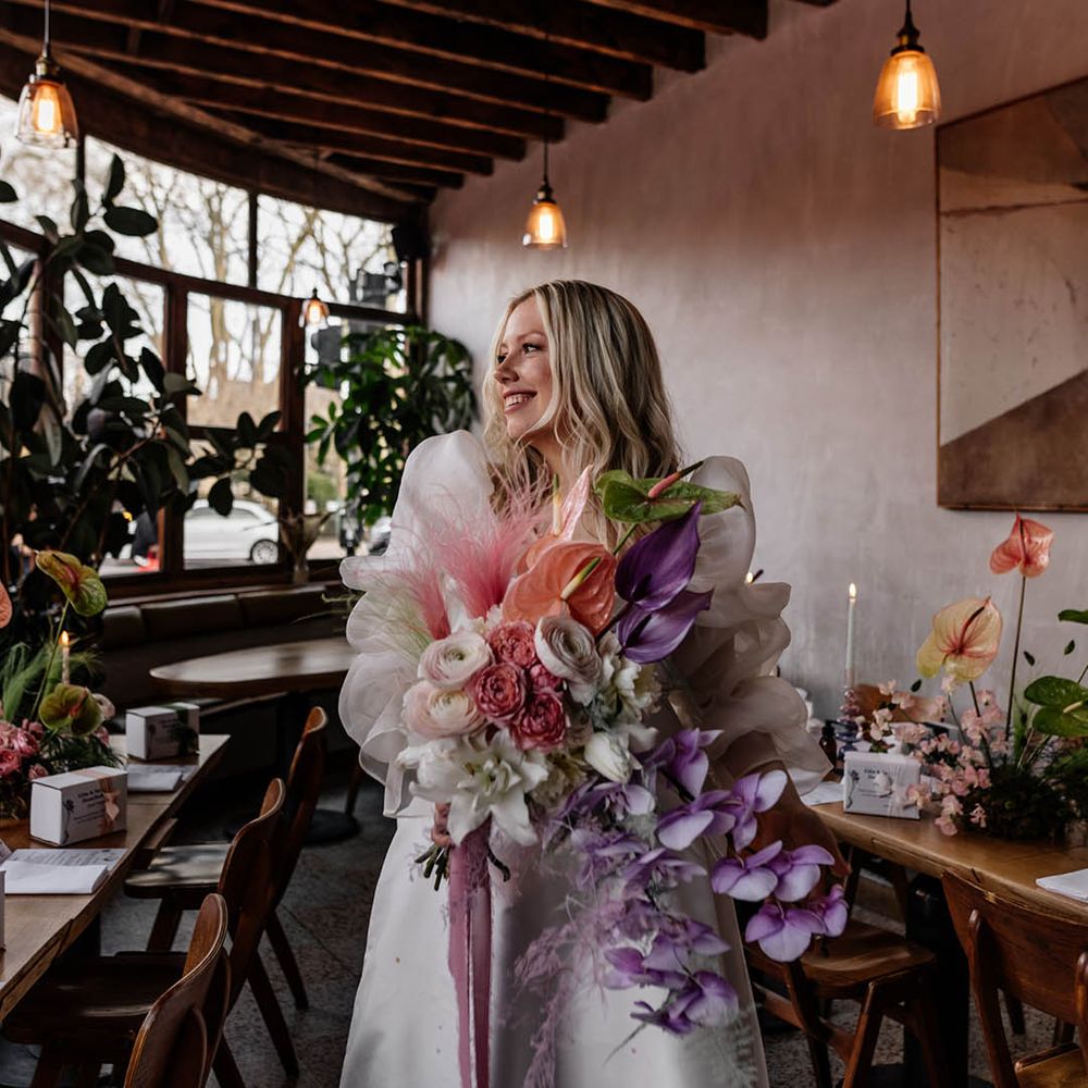 Bride in a JESUS PEIRO wedding dress with voluminous sleeves holding a pastel pink, lilac and white wedding bouquet with orchids, anthuriums and ranunculus flowers