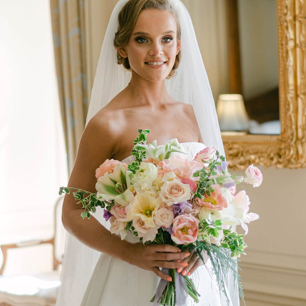 Bride wearing a beaded headband in a strapless wedding dress with coral pink wedding nails holding a pastel bouquet 