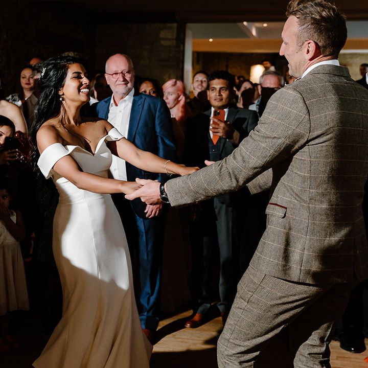 Groom in a brown checkered suit has his first dance with the bride in a fitted wedding dress