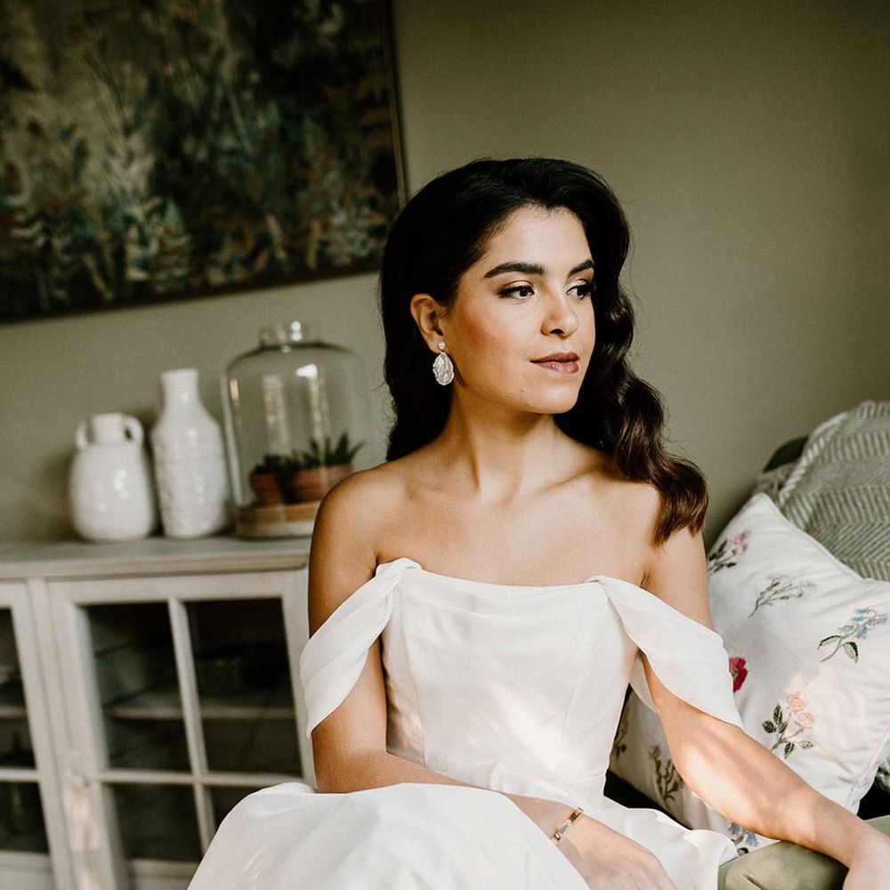 Bride in a structured wedding dress with pearl earrings and her hair styled in Hollywood waves