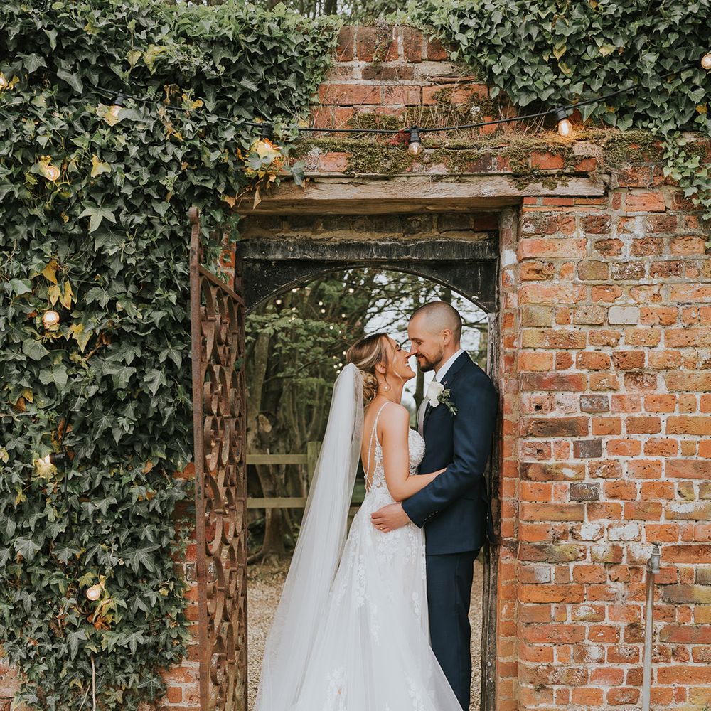Bride in a floral lace wedding dress with a long train and veil with the groom in a dark blue wedding suit 