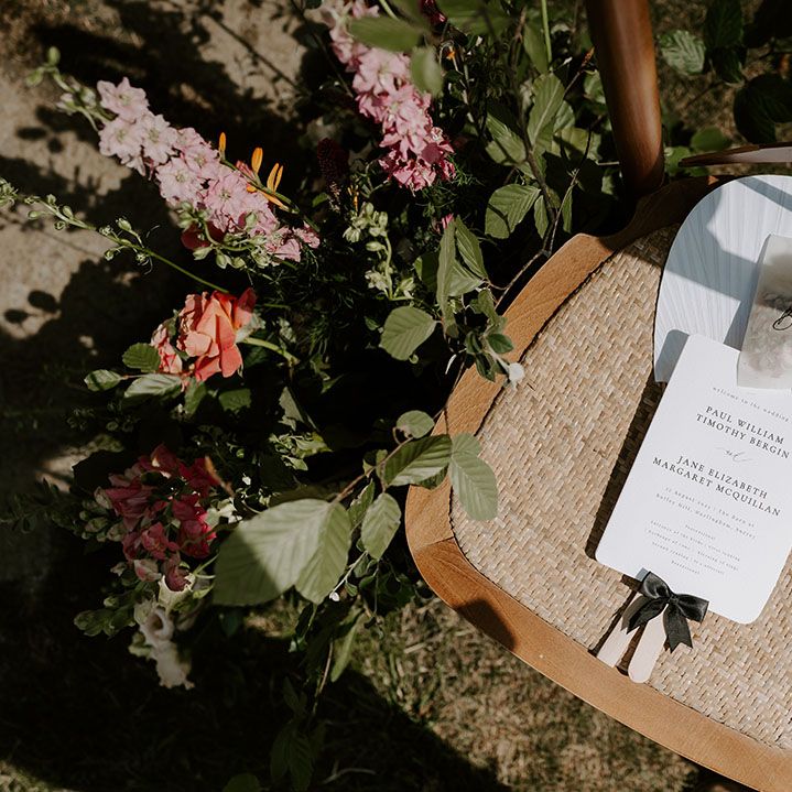 White stationery and fan complete with small bag of confetti on wicker chair outdoors
