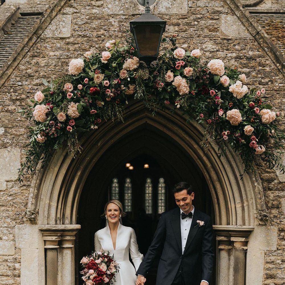 Pink hydrangeas and roses in a flower arch decorate the entrance to the church as the bride and groom exit as a married couple 