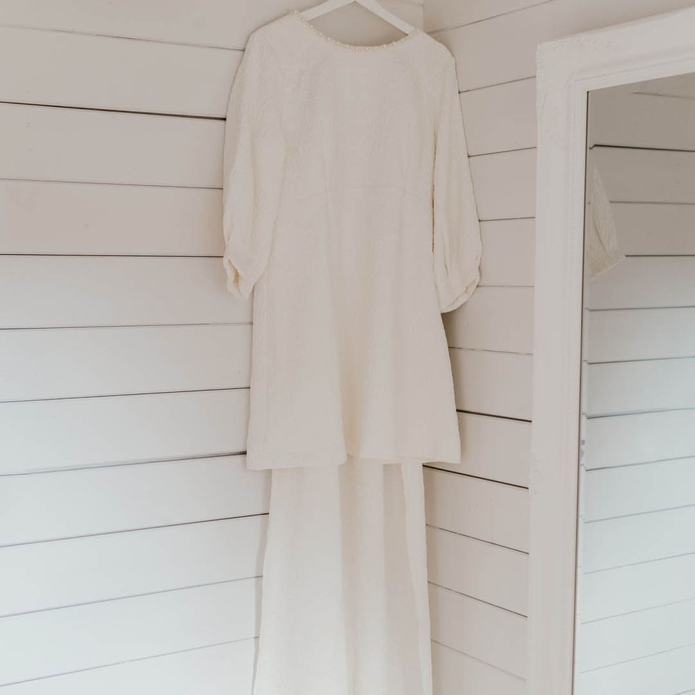 The bride's short wedding dress with bow and long sleeves from Sister Jane hanging on white personalised hanger 