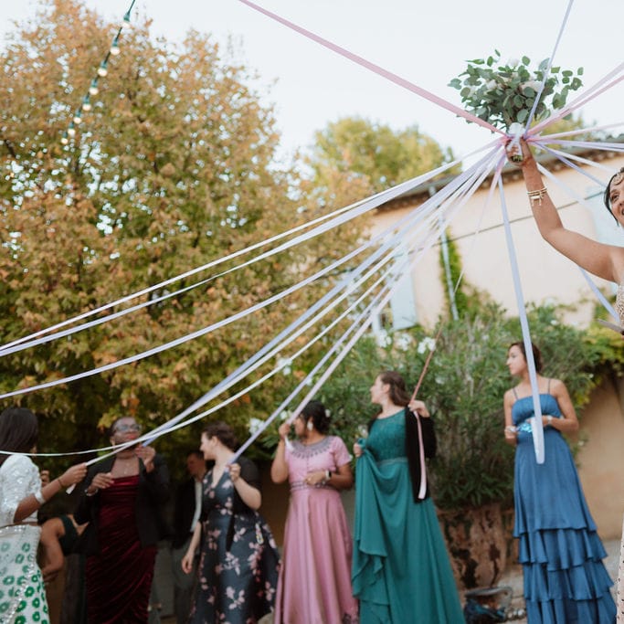 bride in a sparkly gold dress holding up her bouquet with ribbons attached 
