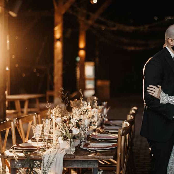Bride in open back silver sparkly wedding dress and groom in classic black tuxedo standing beside contemporary modern luxe wedding tablescape at Elmley Nature Reserve 