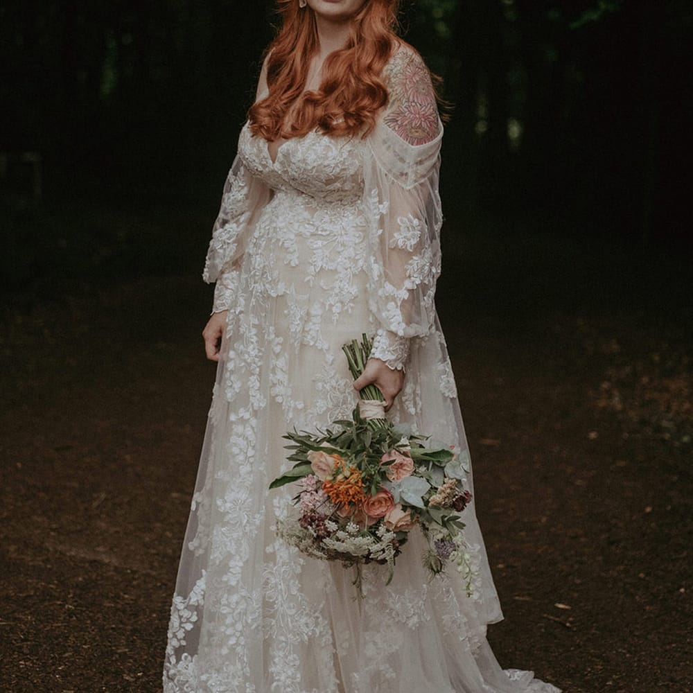 Bride in stunning off the shoulder long sleeve floral lace wedding dress with pink flower crown and matching bridal bouquet 