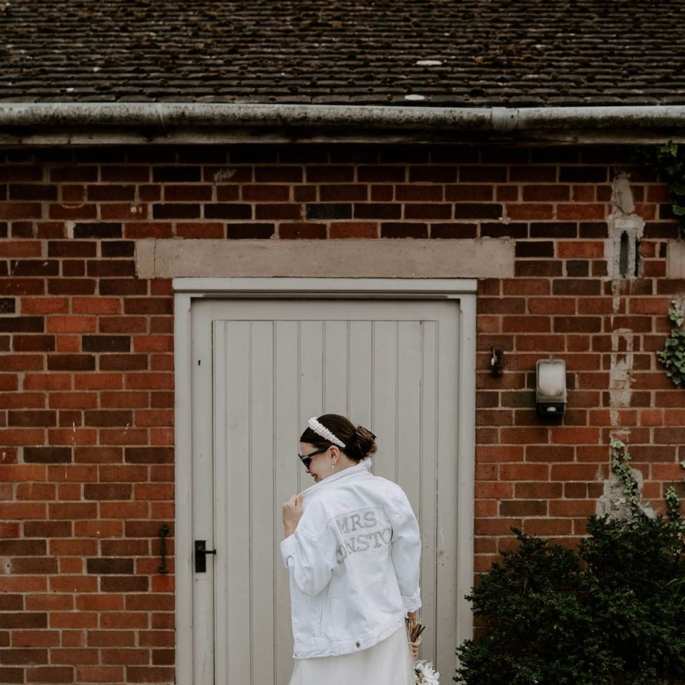 Bride in pearl headband and white denim jacket with personalised pearl name on the back of the jacket with black sunglasses 