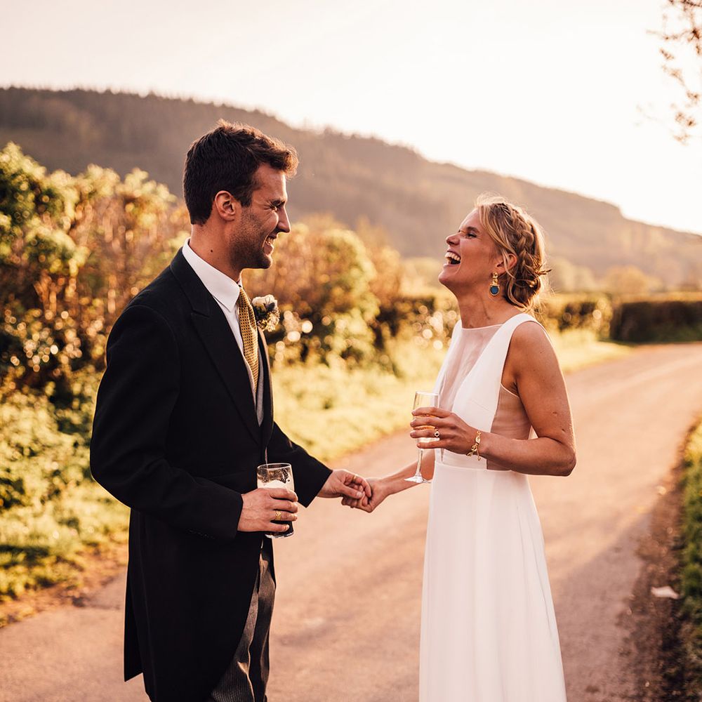 The bride wearing a classic white wedding dress with blue and gold earrings smiling with the groom 