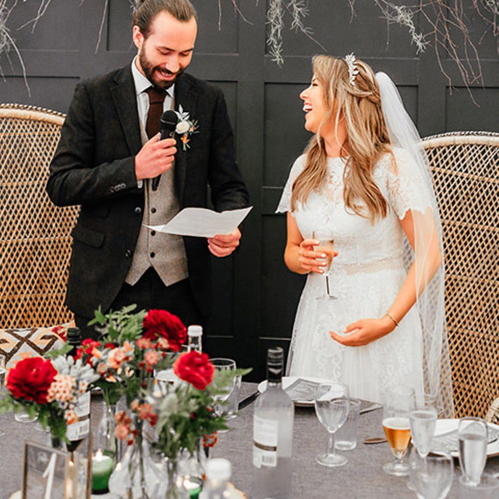 The bride and groom stand in front of the peacock chairs as they read out their wedding speeches 