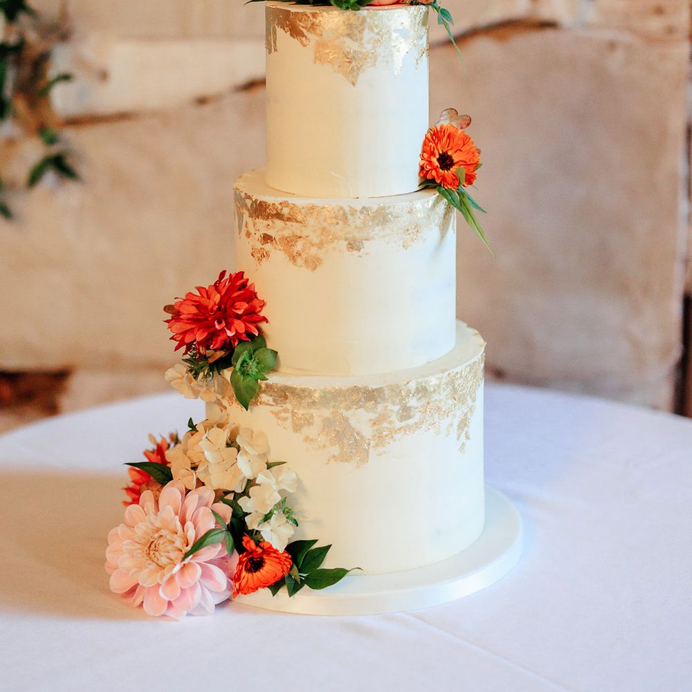 Three tier white iced wedding cake with gold flakes with pink flower decorations 