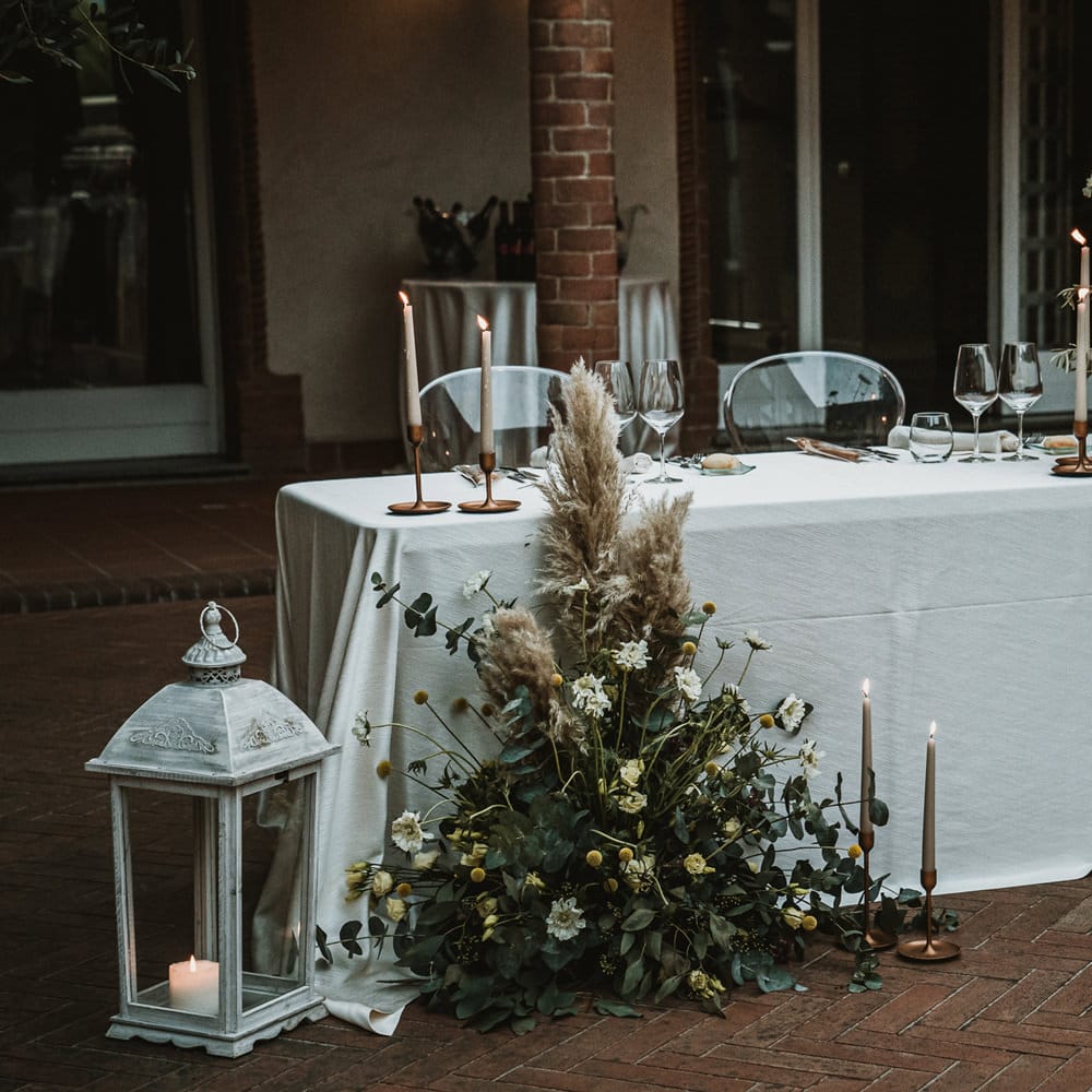 Sweetheart table with ghost chairs, candles, lanterns and pampas grass floral arrangement 