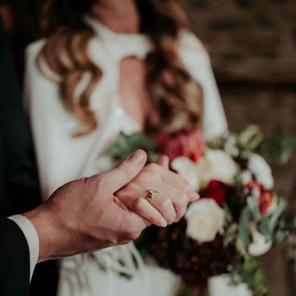The groom holding the brides hand, her wedding ring prominently displayed