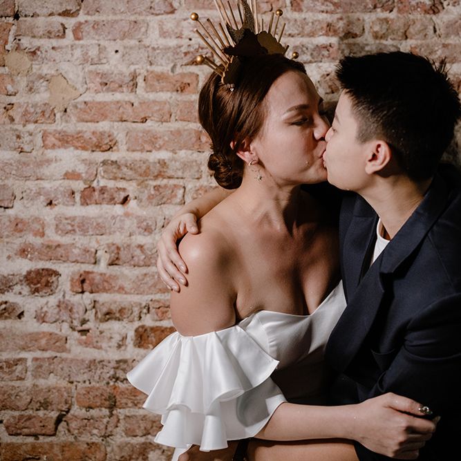 Asian Lesbian wedding with bride in a strapless wedding dress and celestial headdress kissing her partner in a navy suit jacket 