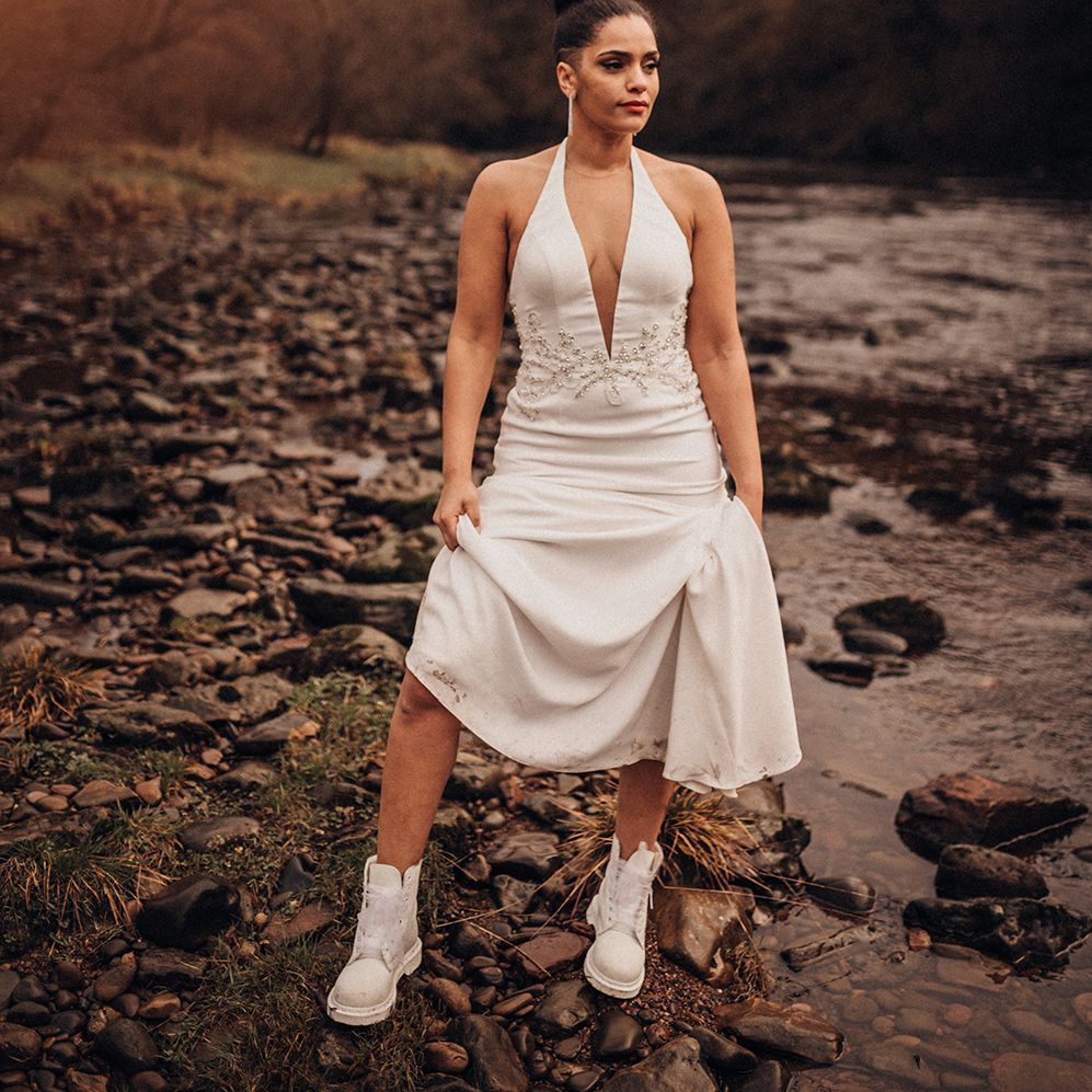 Bride stands outdoors as she lifts wedding gown and wears white Dr Martens