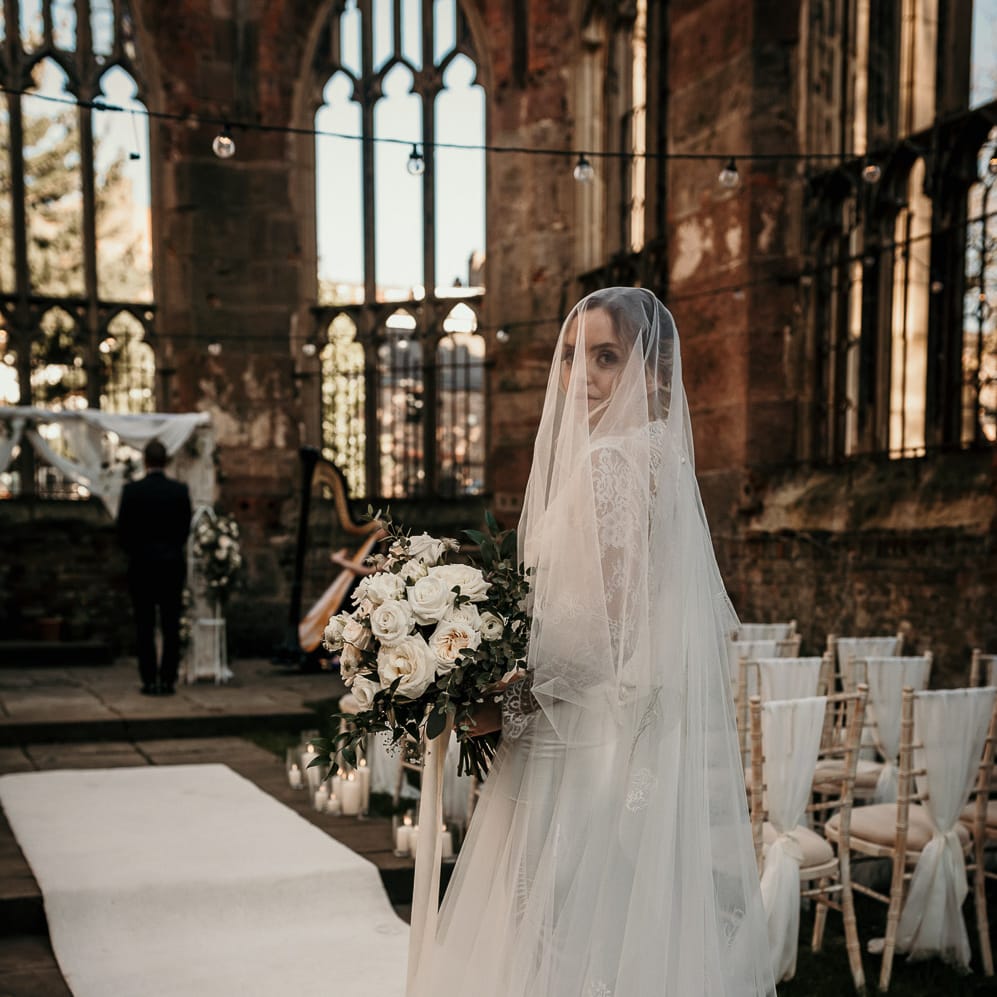Bride in an appliqué cathedral length veil about to walk down the bombed out church aisle 