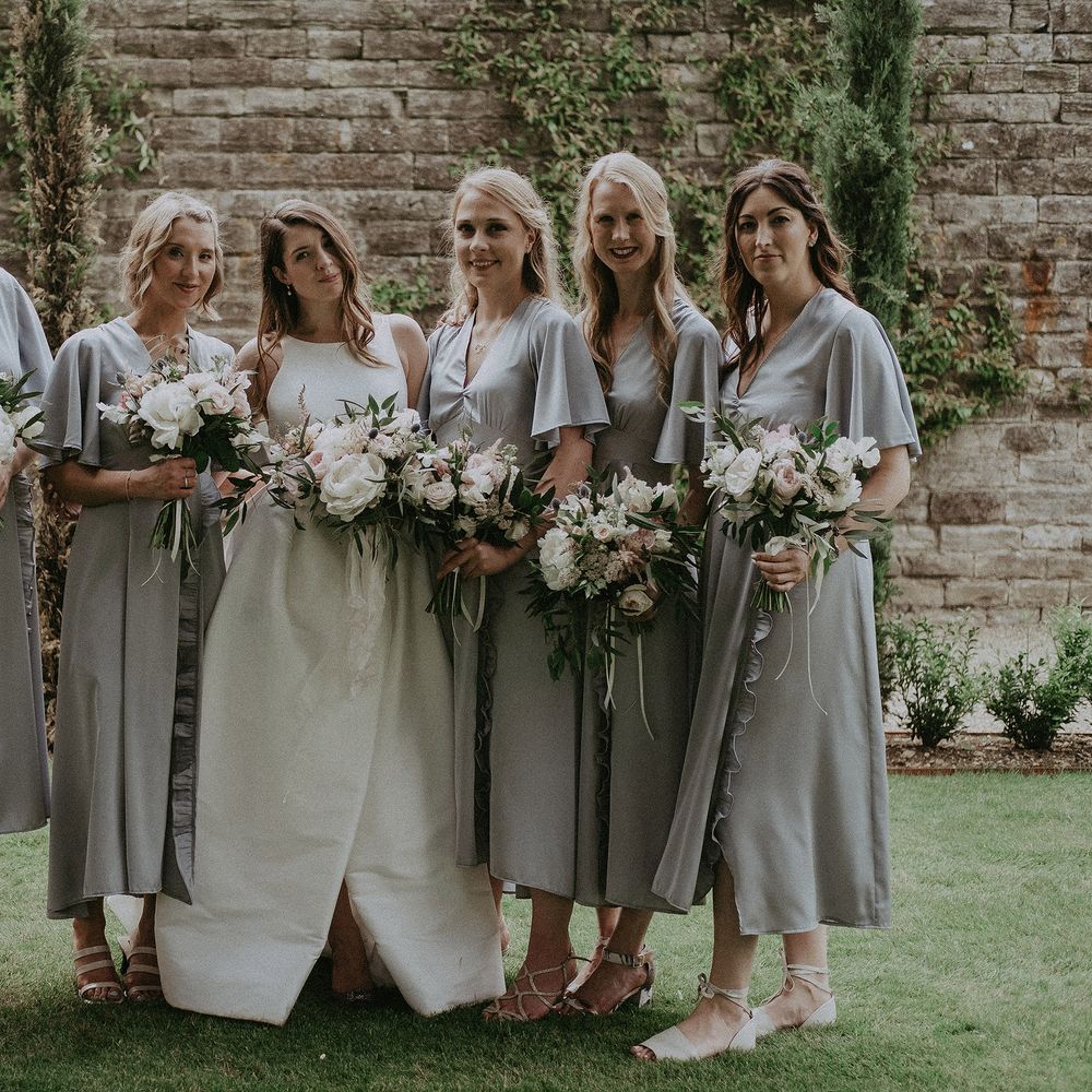 Bride stands with her bridesmaids who wear handmade dresses with batwing sleeves and split front skirt