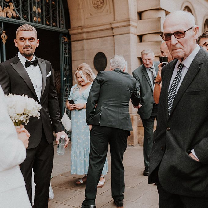 Groom in a tuxedo and wedding guests gathered outside Sheffield Registry Office 