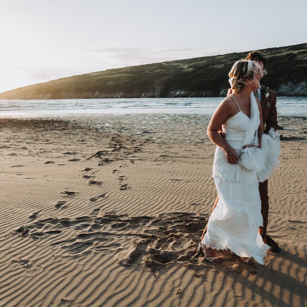 Bride & groom walk along the beach with one another in Cornwall