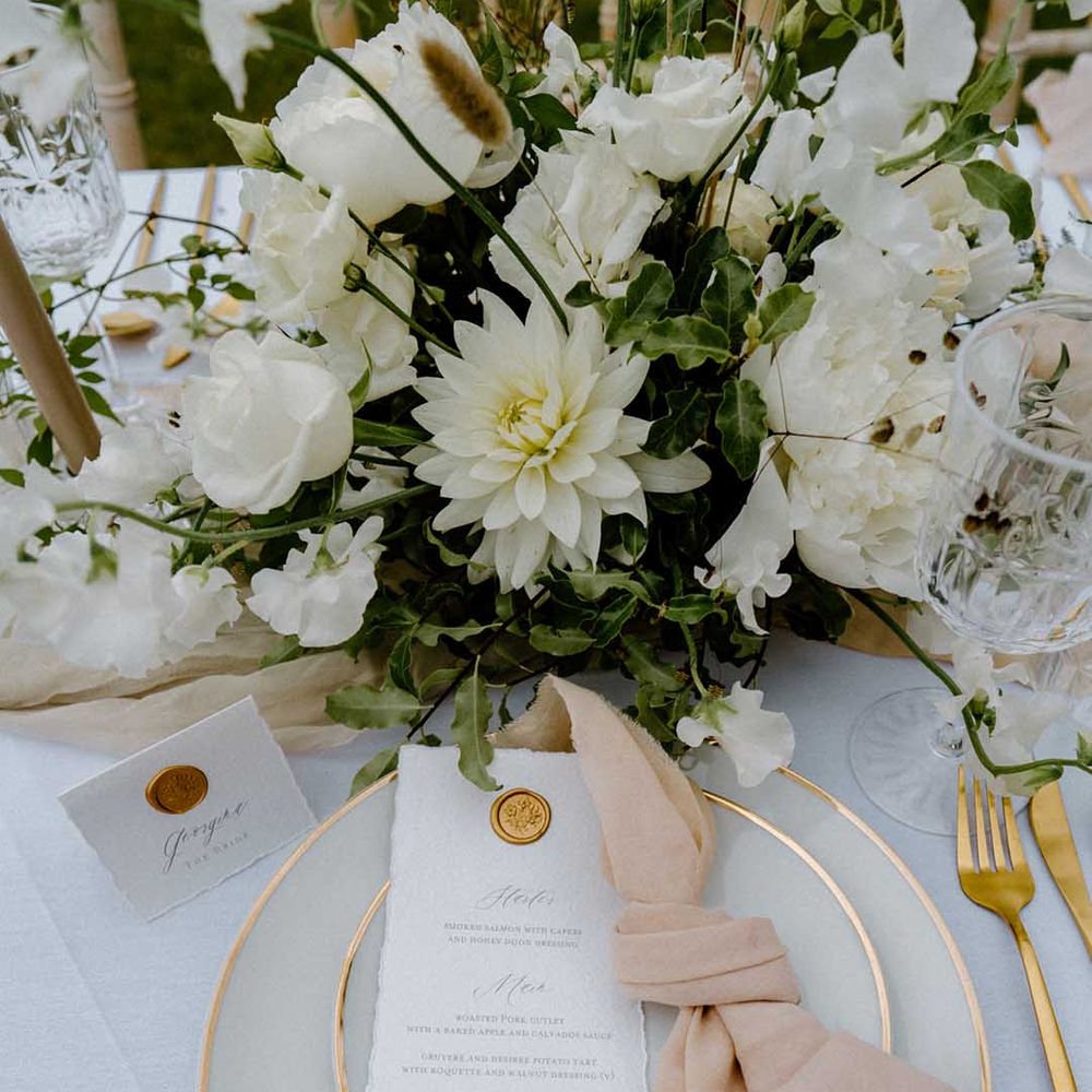 Place setting with gold rimmed tabled ware, gold cutlery and white and green floral centrepiece