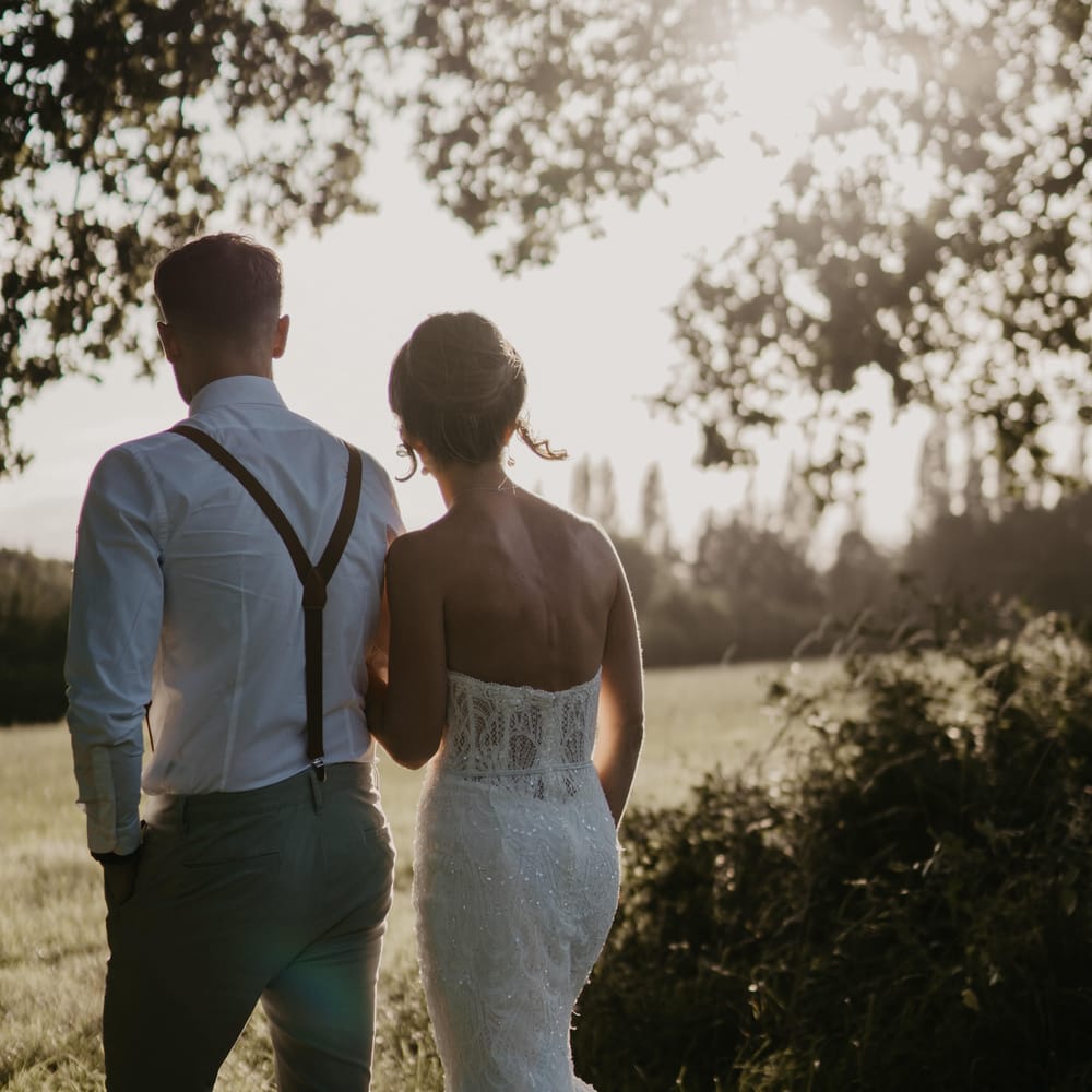 Bride & groom walk together across field as the sun begins to set on their wedding day | Mark Bamforth Photography
