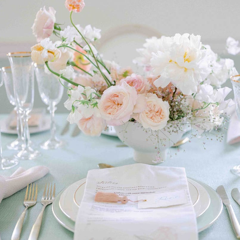 Place setting with pale green tablecloth, gold rimmed glasses and tableware, and floral centrepiece 