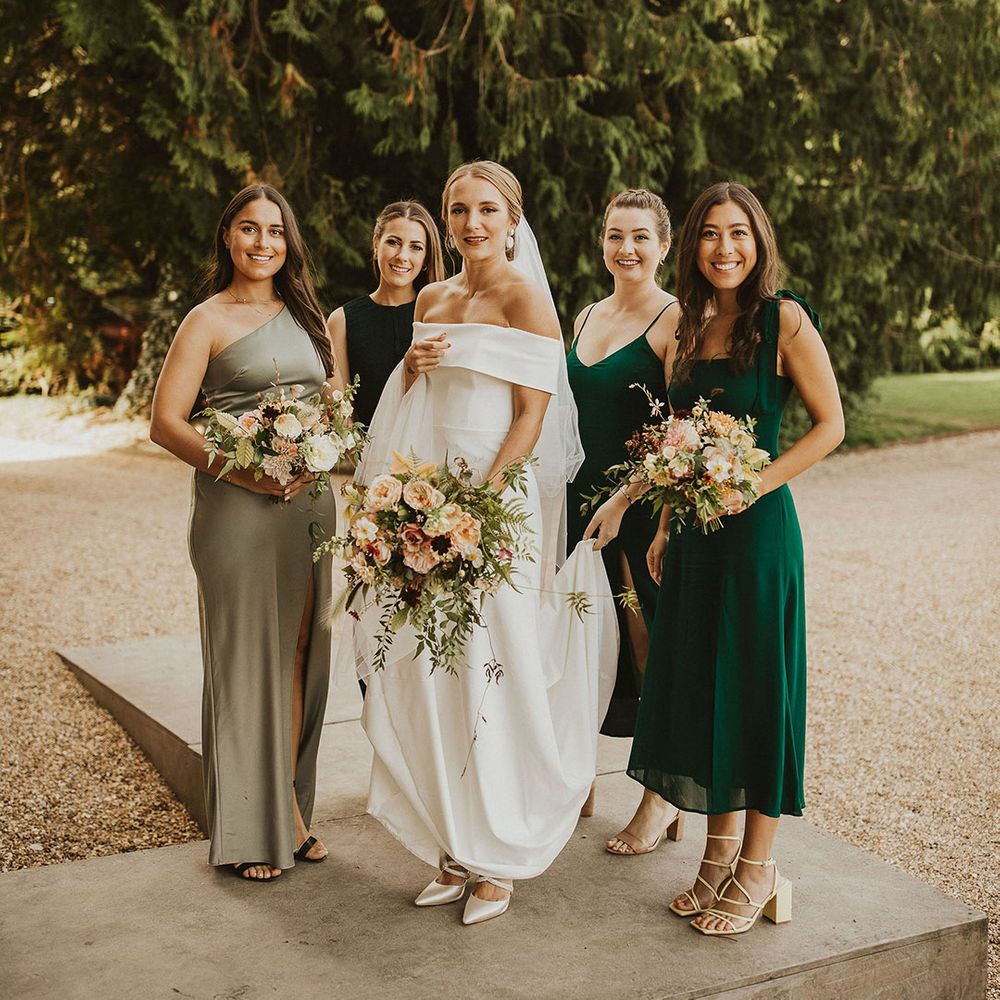 Bride stands with her bridesmaids who wear green bridesmaids gowns in different shades and styles