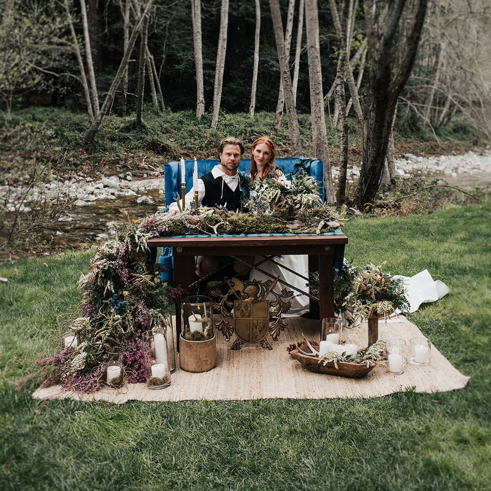Bride with red hair and groom sitting at their outdoor boho sweetheart table 