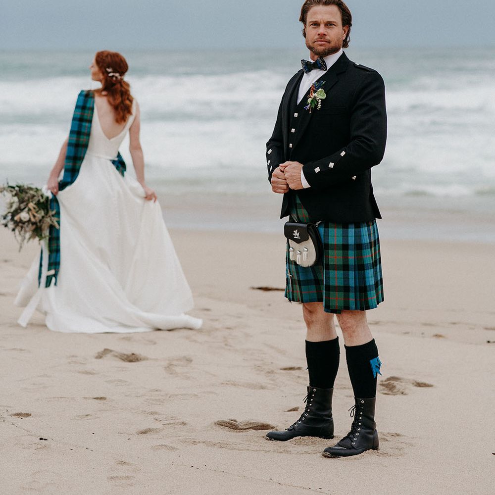 Groom in a blue and green tartan kilt wearing a sporran and black jacket on the beach at Big Sur