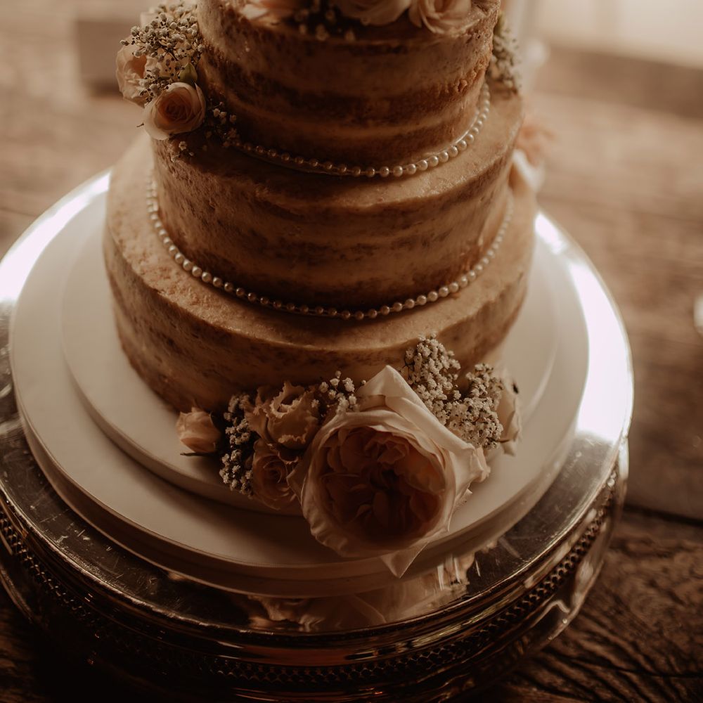 Three tier naked wedding cake decorated with pearls and fresh flowers 
